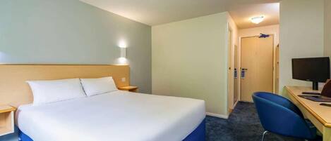 A hotel room with a large bed, a desk with a computer, and a chair.