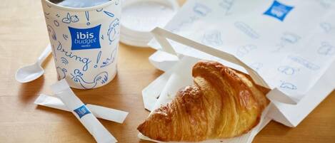 A cup of coffee, a croissant, and a menu on a wooden table.