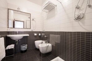 Un baño con un lavamanos blanco, dos inodoros, un espejo y una ducha.