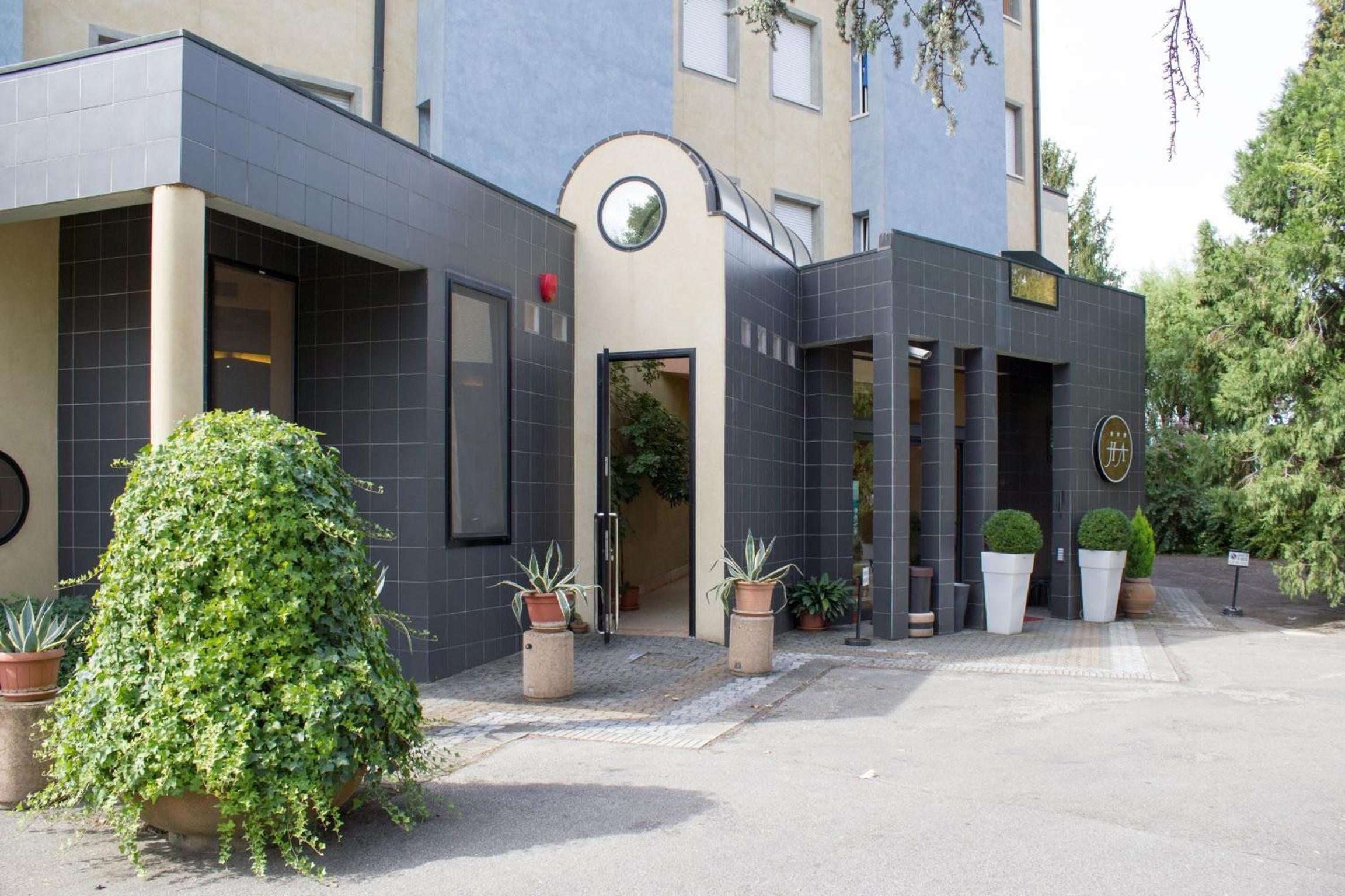 A modern building with a curved entrance, potted plants, and a sign with a logo.