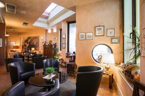 Un vestíbulo de hotel con techo alto, tragaluz, chimenea y una variedad de cuadros enmarcados en las paredes.