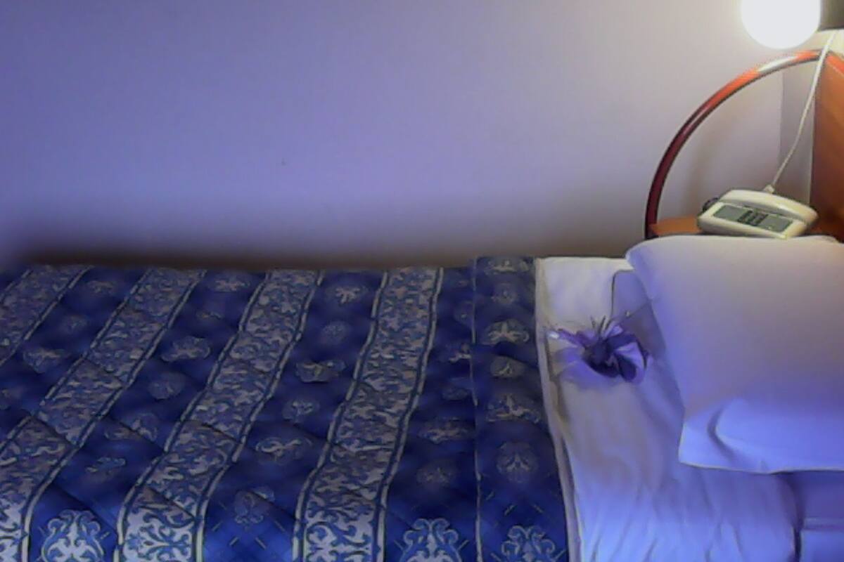 A bedroom with a bed, a bedside table with a lamp, and a digital clock.