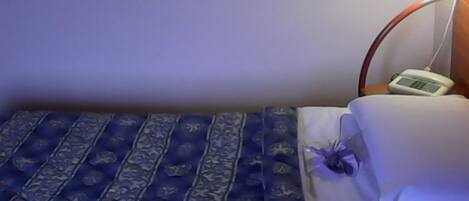 Un dormitorio con una cama, una mesita de noche con lámpara y un reloj digital.
