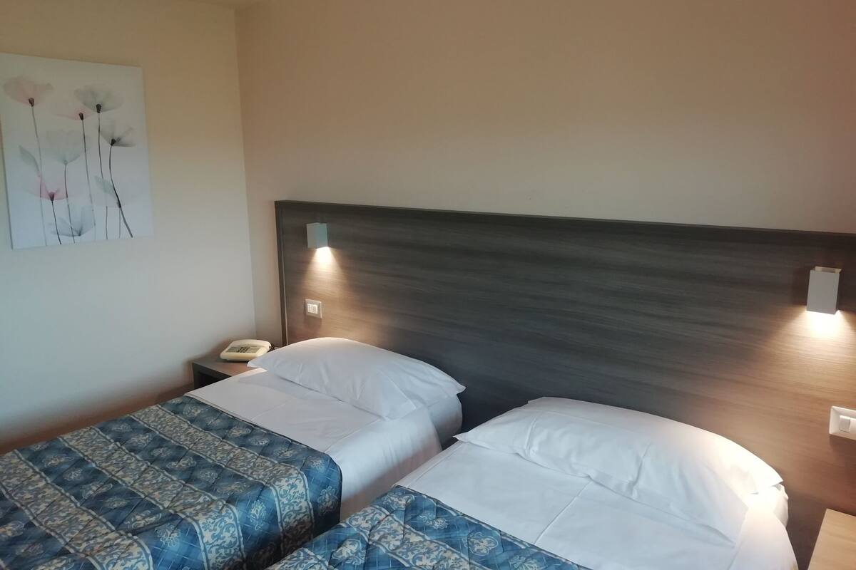 A hotel room with two beds, a nightstand with a telephone, and a wall-mounted light fixture.