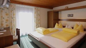 A hotel room with a wooden headboard, two beds with yellow towels, a wooden desk, and a chair. - Pension Stefanie (Soelden)