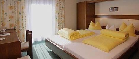 A hotel room with a wooden headboard, two beds with yellow towels, a wooden desk, and a chair.