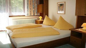 A bedroom with a bed, two pillows, a nightstand with a lamp, a framed picture on the wall, and a window with curtains. - Pension Stefanie (Soelden)