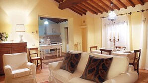A cozy living room with a white sofa, two armchairs, a wooden cabinet, and a dining area with a table and chairs. - I Grandi Di Toscana (Civitella in Val di Chiana)