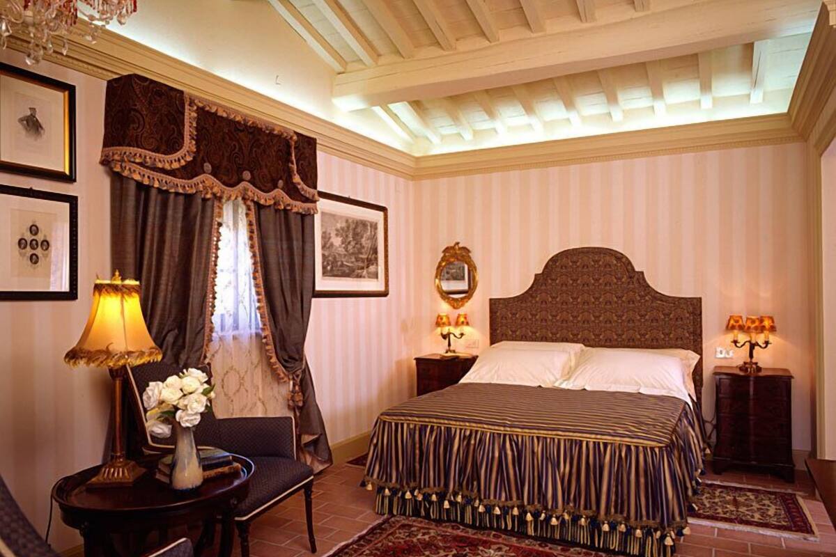 Ein Hotelzimmer mit einem großen Bett, zwei Nachttischen, einer Deckenleuchte, einem Schreibtisch mit Stuhl und einem großen Fenster mit Vorhängen.