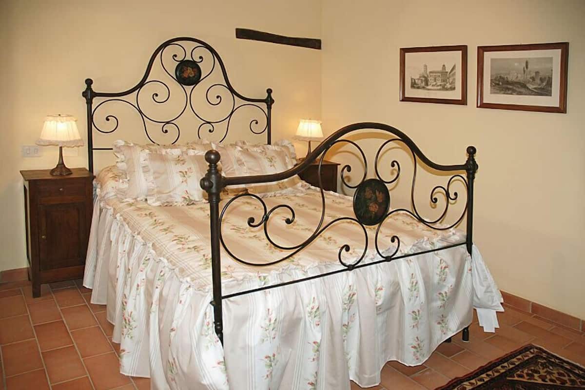Ein Schlafzimmer mit einem Metallbettgestell, einem blumigen Bettüberwurf, zwei Nachttischen mit Lampen und gerahmten Bildern an der Wand.