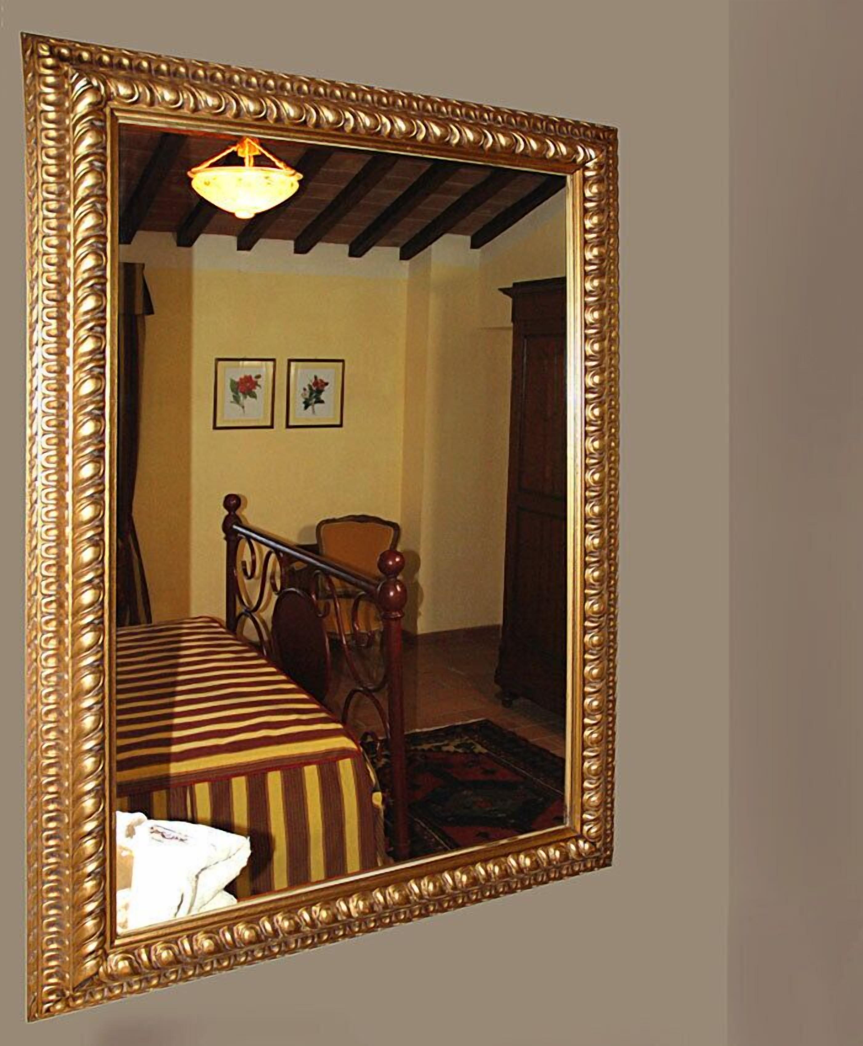 A bedroom with a large ornate mirror, a bed with striped bedding, a chair, and a small rug.