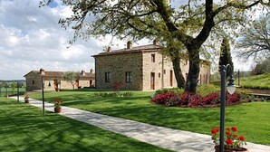 A stone building with a paved pathway leading to it, surrounded by well-maintained grass and flowering plants. - I Grandi Di Toscana (Civitella in Val di Chiana)