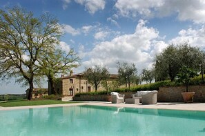 Un espace piscine avec des meubles d’extérieur, un b âtiment en pierre et des arbres.