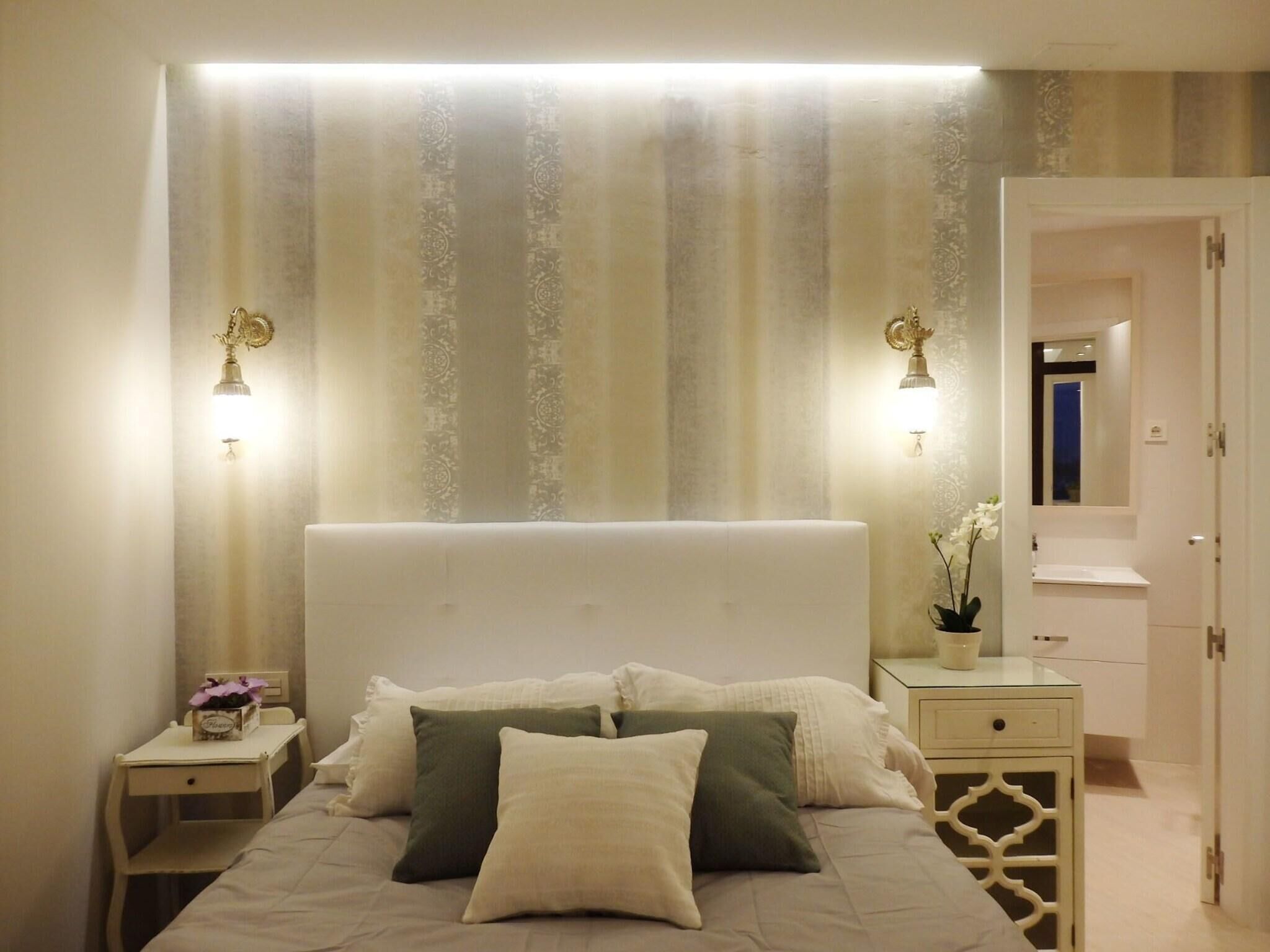 A bedroom with a large bed, two bedside tables, a nightstand, a mirror, and a door leading to a bathroom.