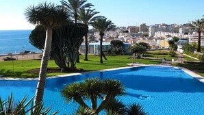 Une piscine bordée de palmiers, offrant une vue sur le paysage urbain de la côte.