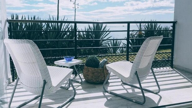 Un balcon avec deux chaises en osier blanches, une petite table ronde et un panier en osier tressé.