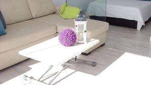 Une pièce moderne et bien éclairée, avec un canapé, une petite table sur laquelle se trouve une lanterne et un objet décoratif, ainsi qu'un lit avec une literie bleue.