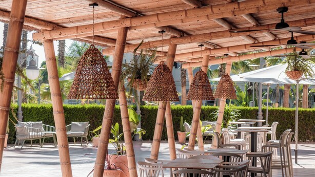 An outdoor cafe with bamboo pillars, hanging woven light fixtures, and white plastic chairs and tables. - Dunas de Doñana (Almonte)