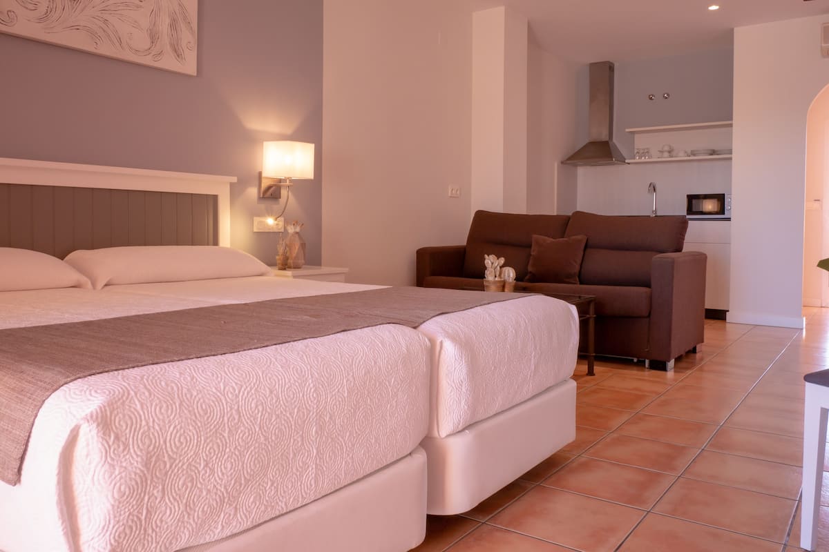 Quarto com uma cama grande, um sofá marrom e uma mesinha com objetos decorativos.