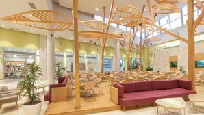 Un vaste espace intérieur aménagé avec différents coins salon, comprenant des tables et des chaises, ainsi qu’un espace central avec un canapé rouge et des structures en bois.