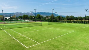 A tennis court with a net, surrounded by green grass and a fence.