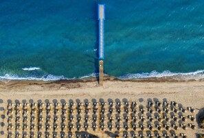 An aerial view of a beach with a long pier extending into the sea and rows of sun loungers. - Blue Lagoon Resort (Kos)