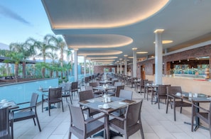 A spacious outdoor dining area with multiple tables and chairs, a poolside view, and a brick wall with a glass display case.