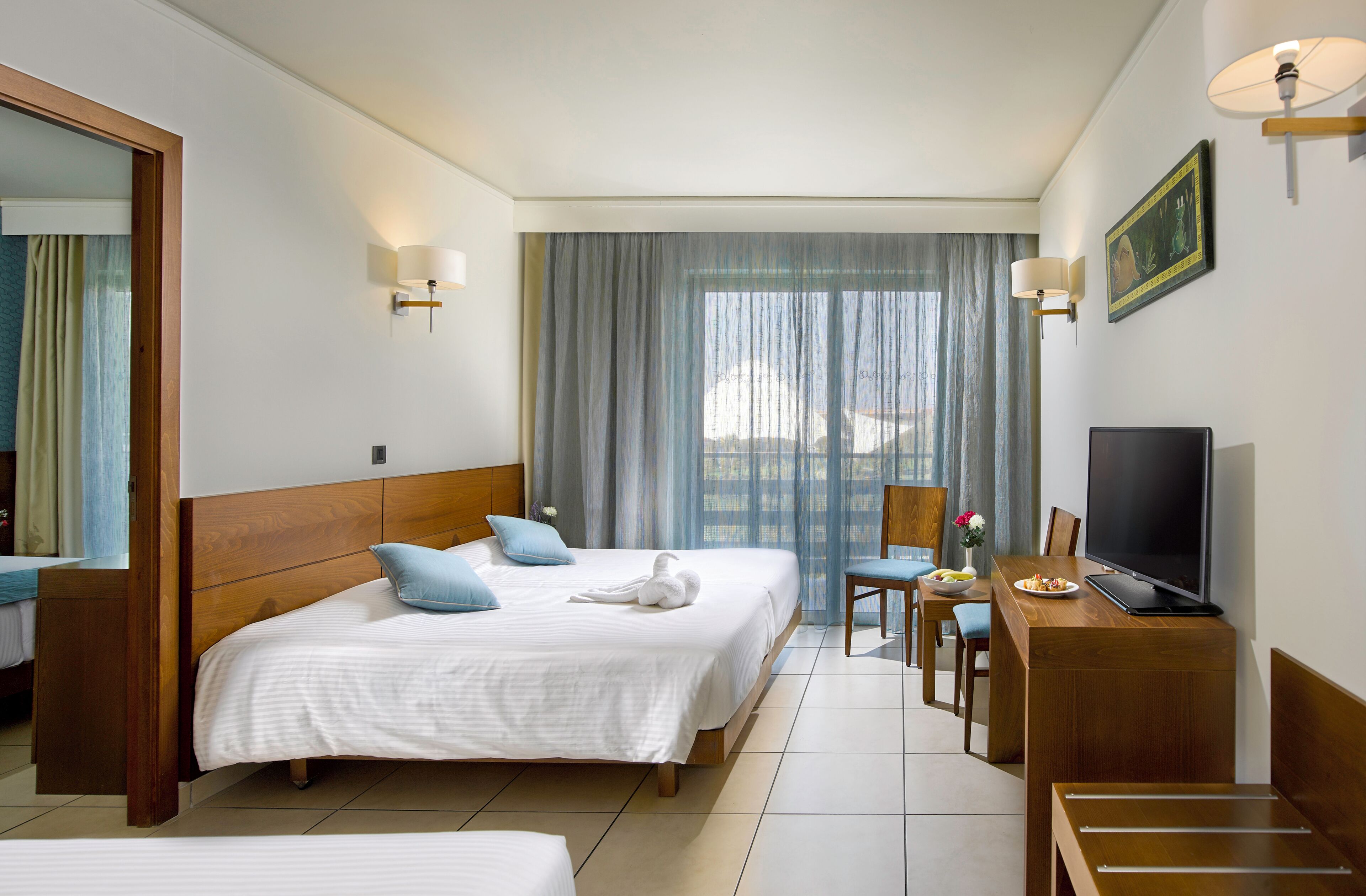 A hotel room with two beds, a desk with a TV, a chair, and a window with curtains.