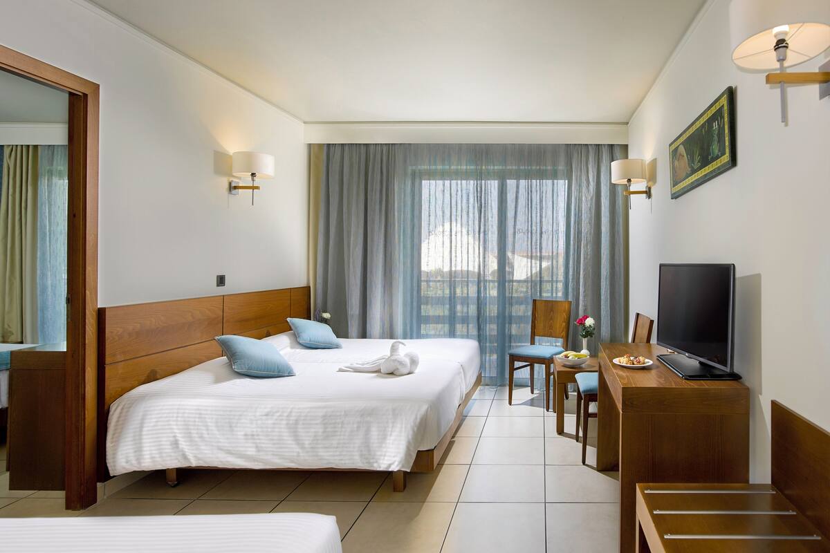 A hotel room with two beds, a desk with a TV, a chair, and a window with curtains.