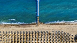 Une vue aérienne d’une plage avec une longue jetée qui s’avance dans la mer et de nombreuses rangées de chaises longues.