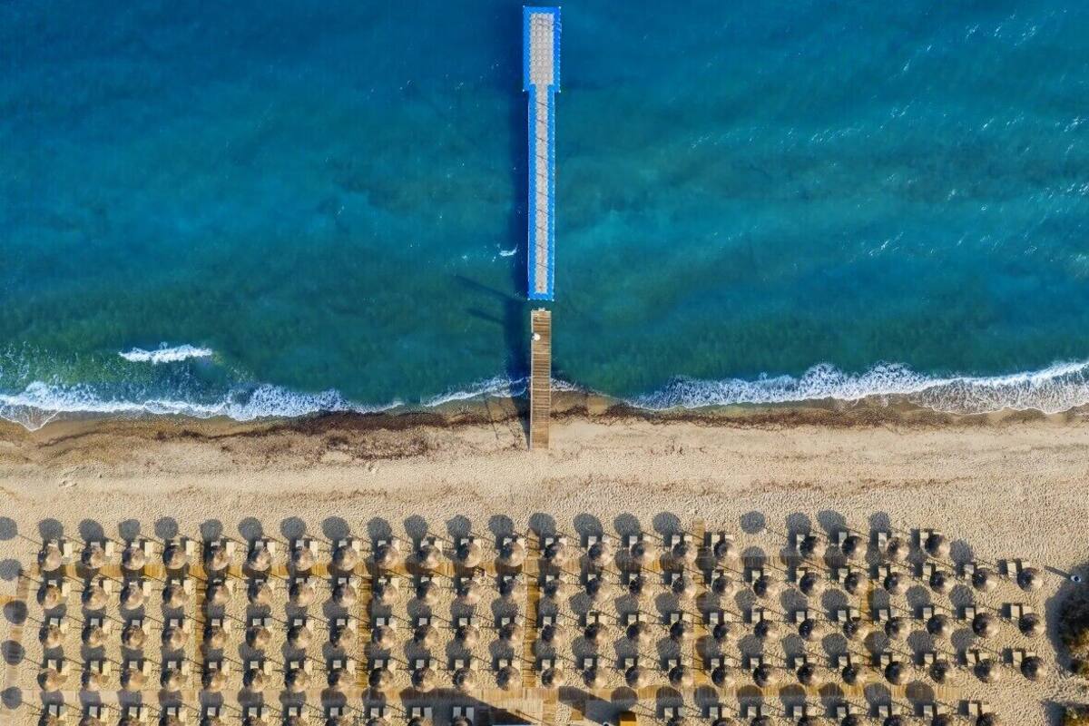 An aerial view of a beach with a long pier extending into the sea and rows of sun loungers.