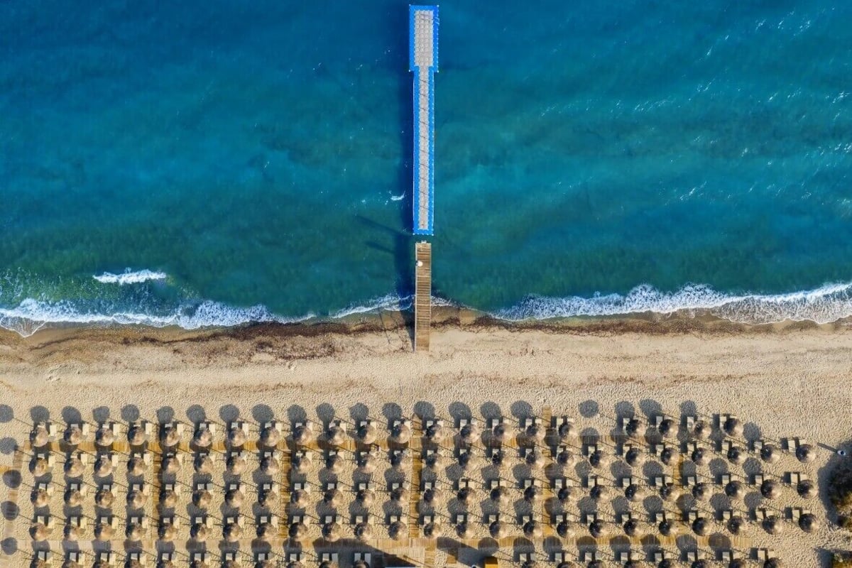 An aerial view of a beach with a long pier extending into the sea and rows of sun loungers.