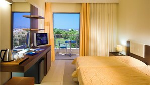 A hotel room with a bed, a desk with a computer, a chair, a balcony with a view, and a window with curtains.