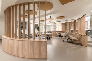 A modern interior with a curved wooden partition, round tables, and a seating area with sofas.