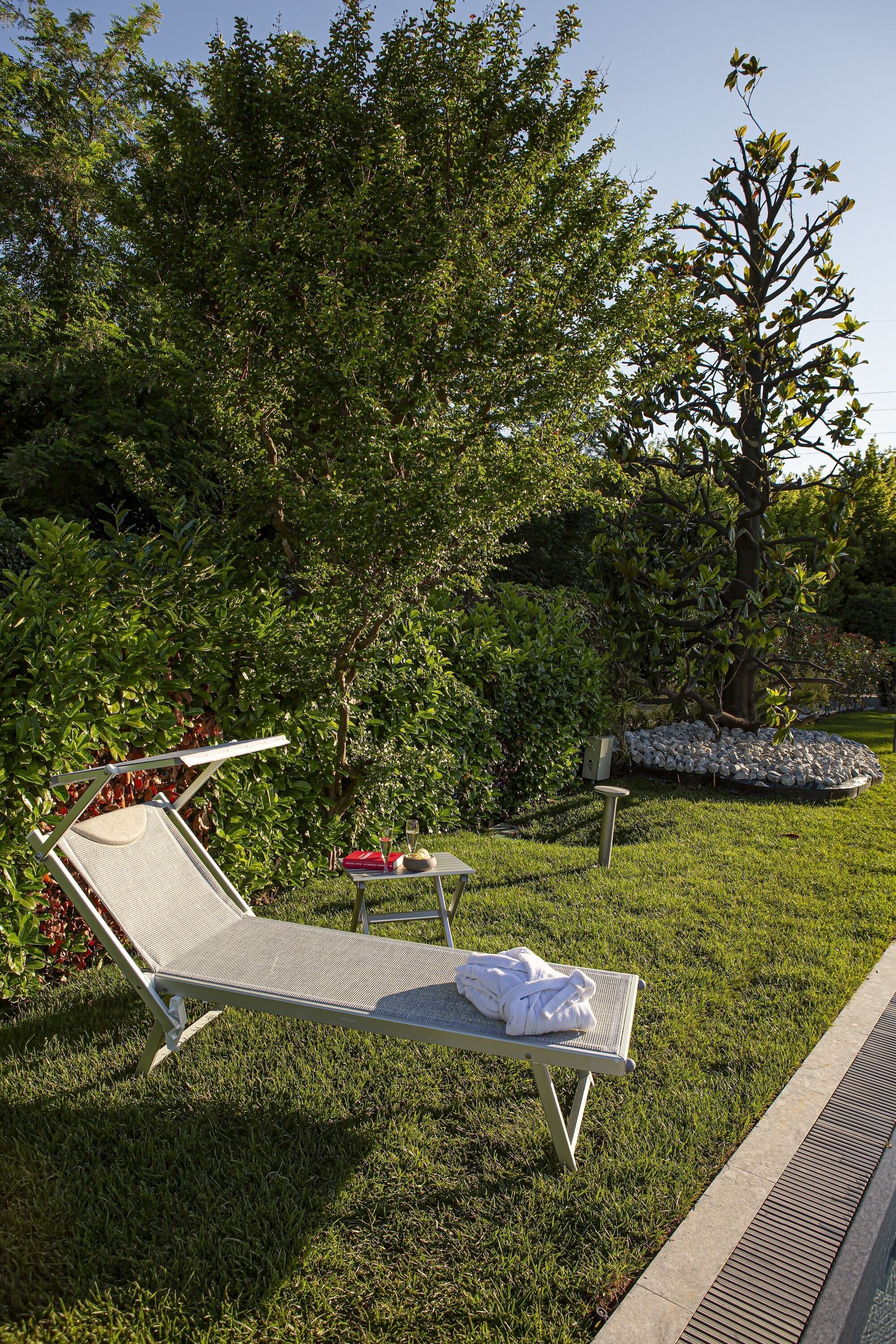 Un jardín con piscina, una silla de descanso y una mesita con una toalla.