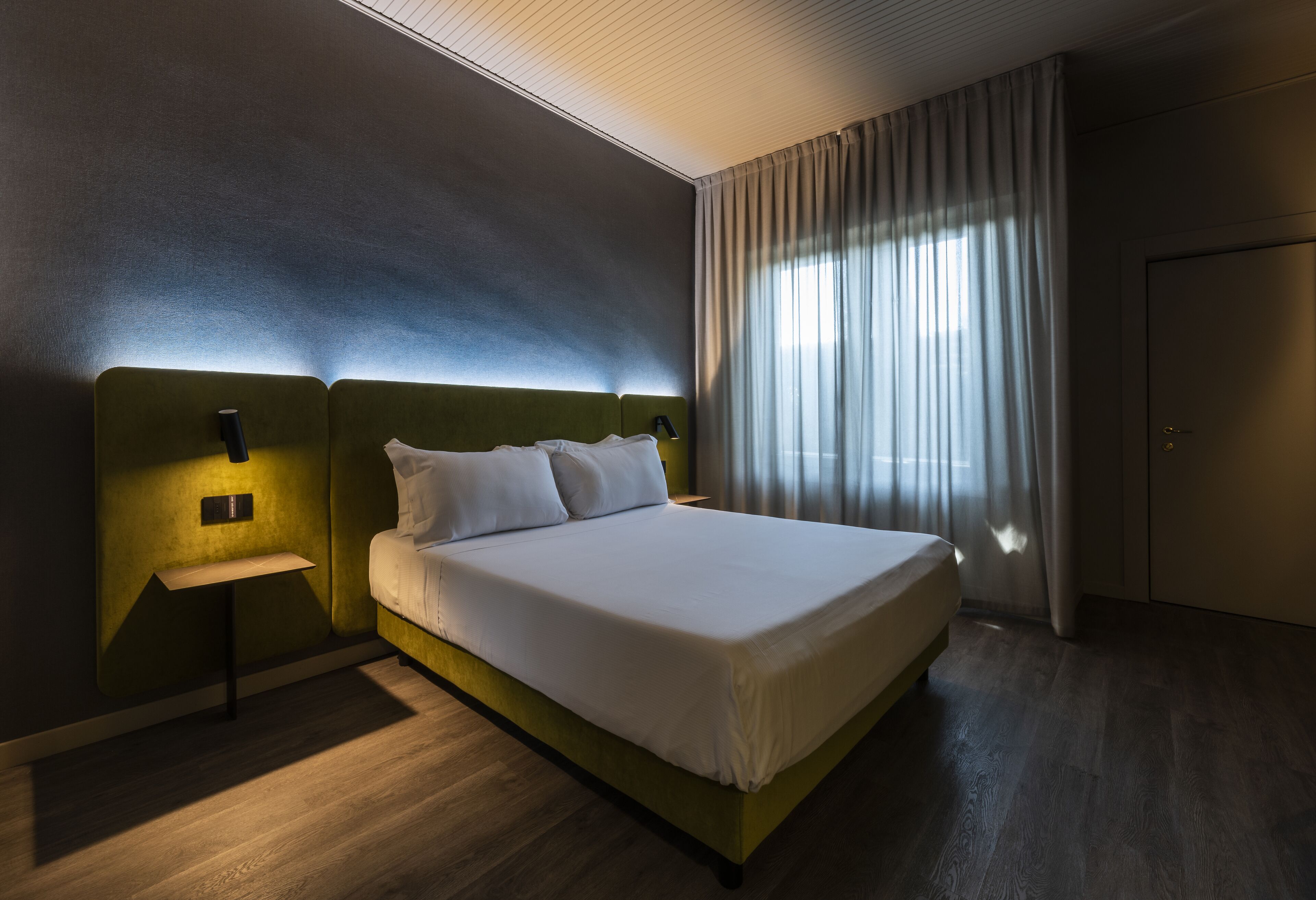 A modern hotel room with a large bed, a bedside table, and a nightstand.