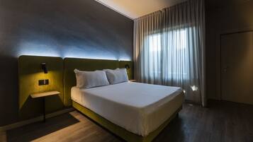 A modern hotel room with a large bed, a bedside table, and a nightstand.