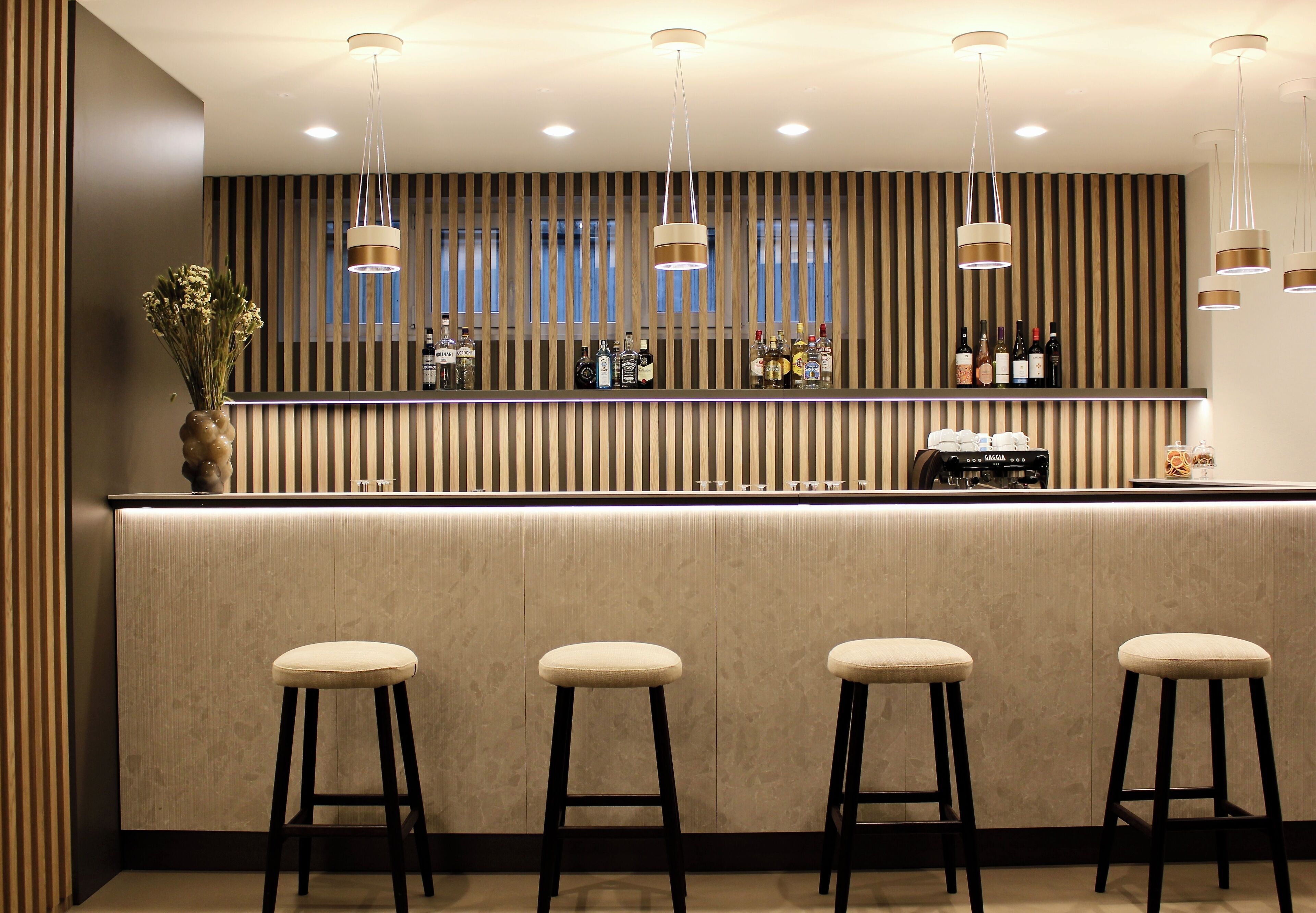 Una zona de bar con mostrador, taburetes, luces colgantes y pared a rayas.