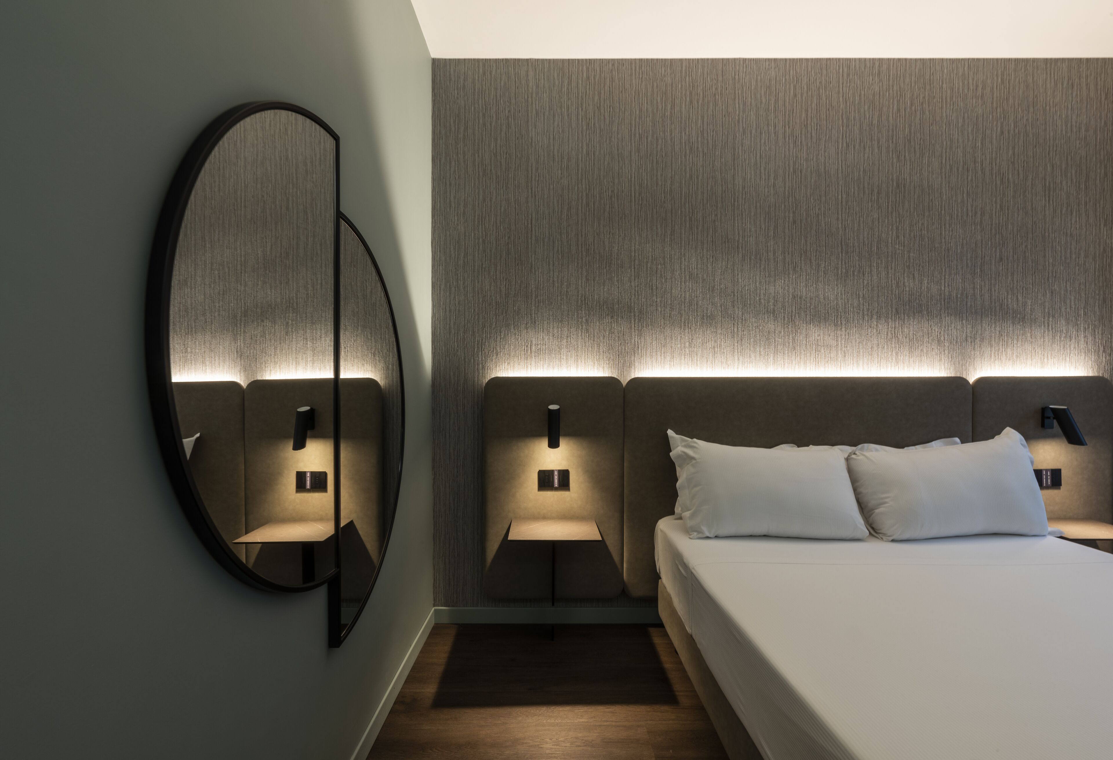 Ein modernes Hotelzimmer mit einem großen Bett, zwei Nachttischen, einem wandmontierten Spiegel und einer strukturierten Wand.
