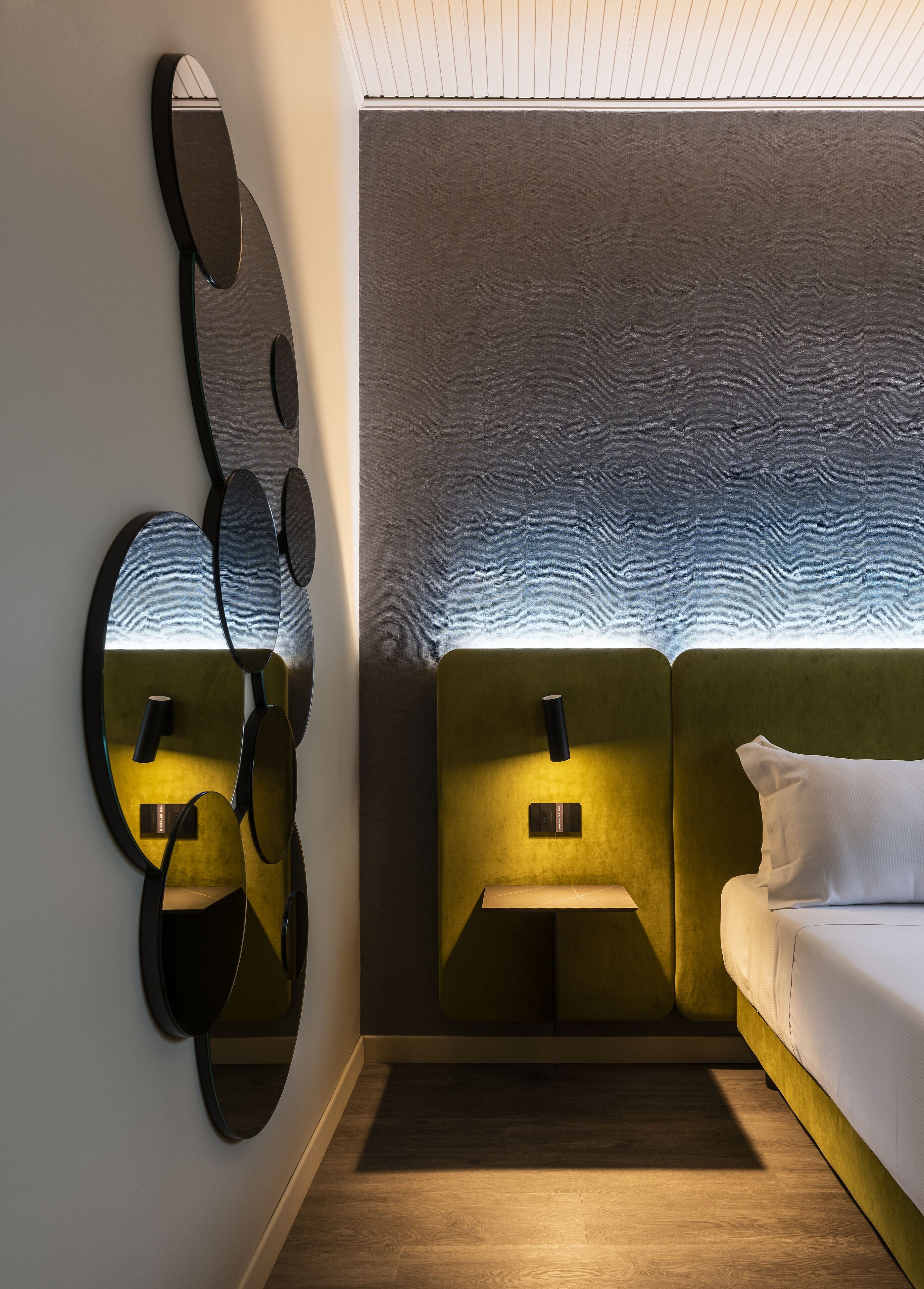 Una habitación de hotel moderna con una obra de arte original en la pared, un cabecero verde y una mesita de noche con lámpara.