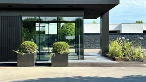 A modern building with a glass entrance, two potted plants, and a clear blue sky. - Hotel Mealba Suite & Pool (Saronno)