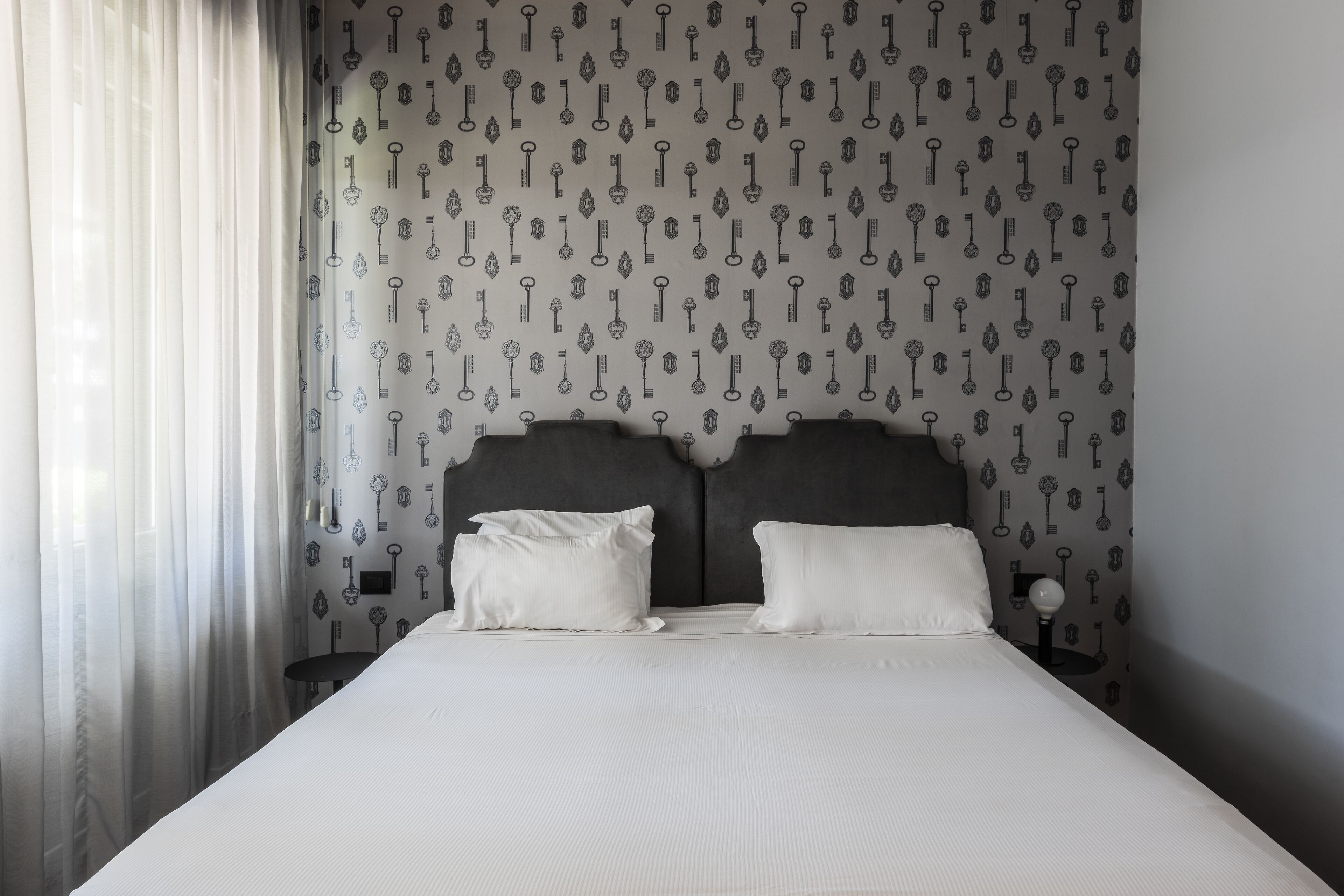 A neatly made bed with white linens, a dark headboard, and a wall with a key pattern.