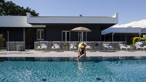 A swimming pool with lounge chairs and umbrellas, a stone wall, and a modern building with a flat roof. - Hotel Mealba Suite & Pool (Saronno)