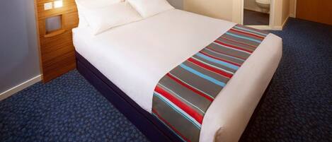 A hotel room with a neatly made bed, a wooden headboard, a blue carpet, and a view of the bathroom.