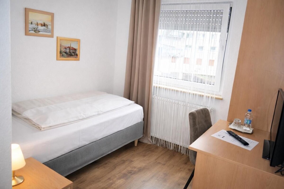 Habitación de hotel con cama, escritorio con silla, televisor y dos cuadros en la pared.