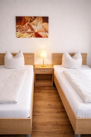A hotel room with two single beds, a bedside table with a lamp, and a painting on the wall. - Hotel Discovery (Stuttgart)