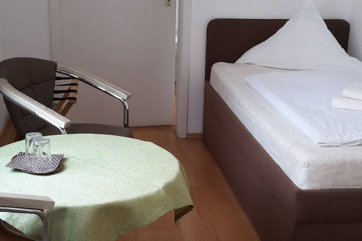 A small, clean room with a bed, a chair, a table, and a door.
