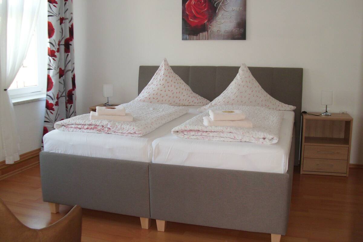 A double bed with a grey headboard, two bedside tables with lamps, and a floral curtain.