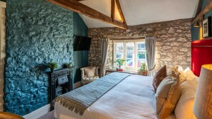 A bedroom with a stone wall, a fireplace, a bed with pillows, and a window with curtains. - The Bowl Inn (Bristol)