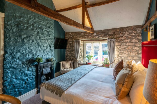 A bedroom with a stone wall, a fireplace, a bed with pillows, and a window with curtains.